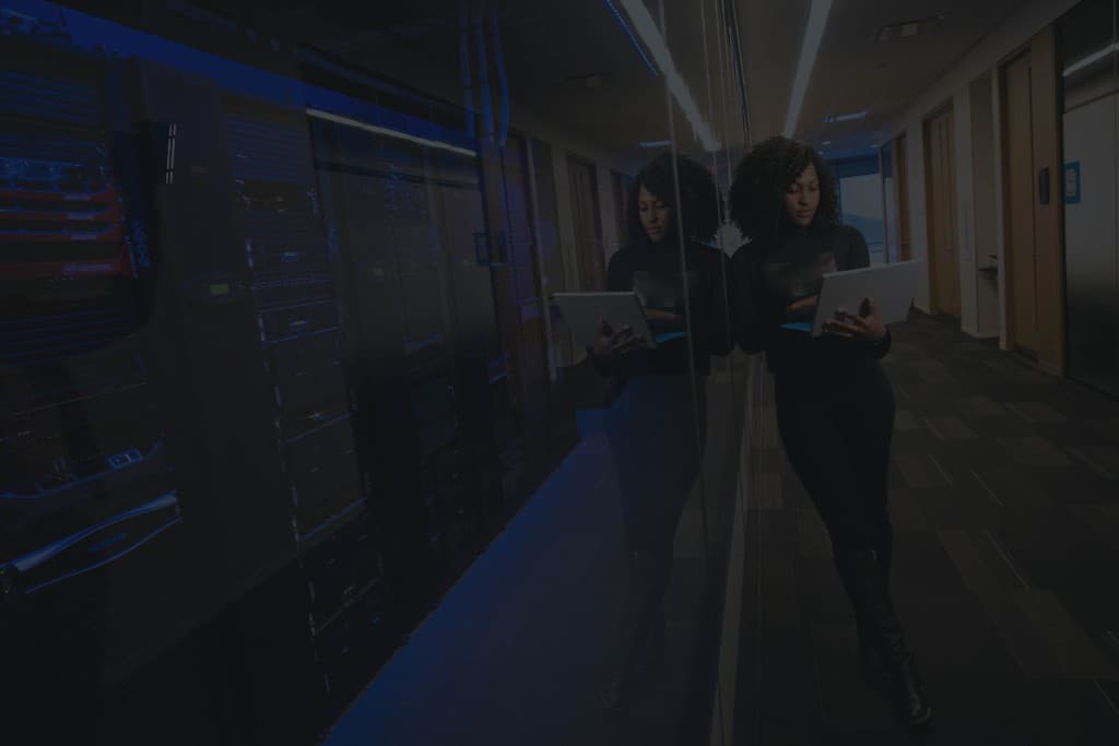 Engineer with a laptop standing beside server racks in a data center hallway