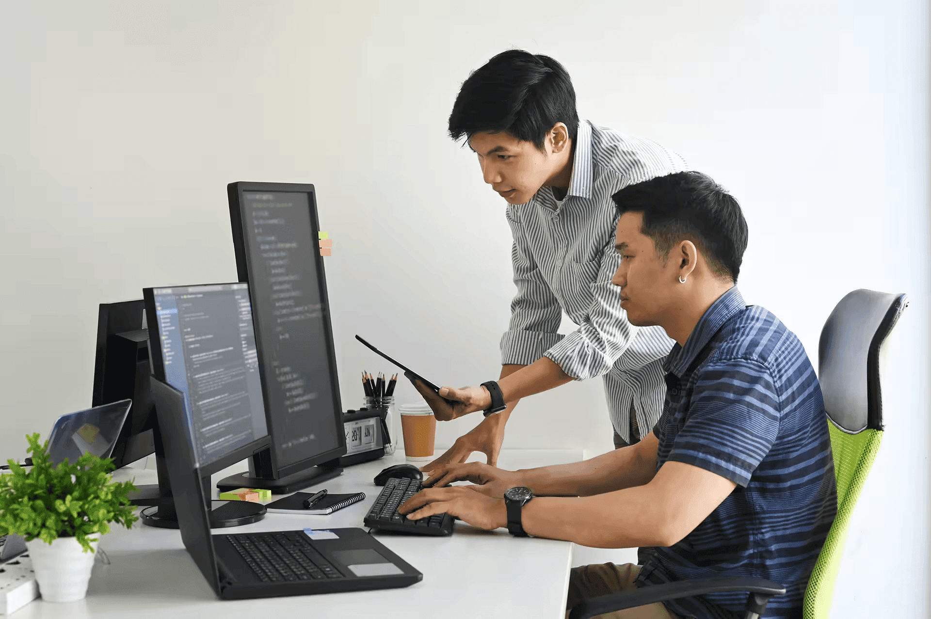 Two engineers reviewing code across multiple monitors at a desk