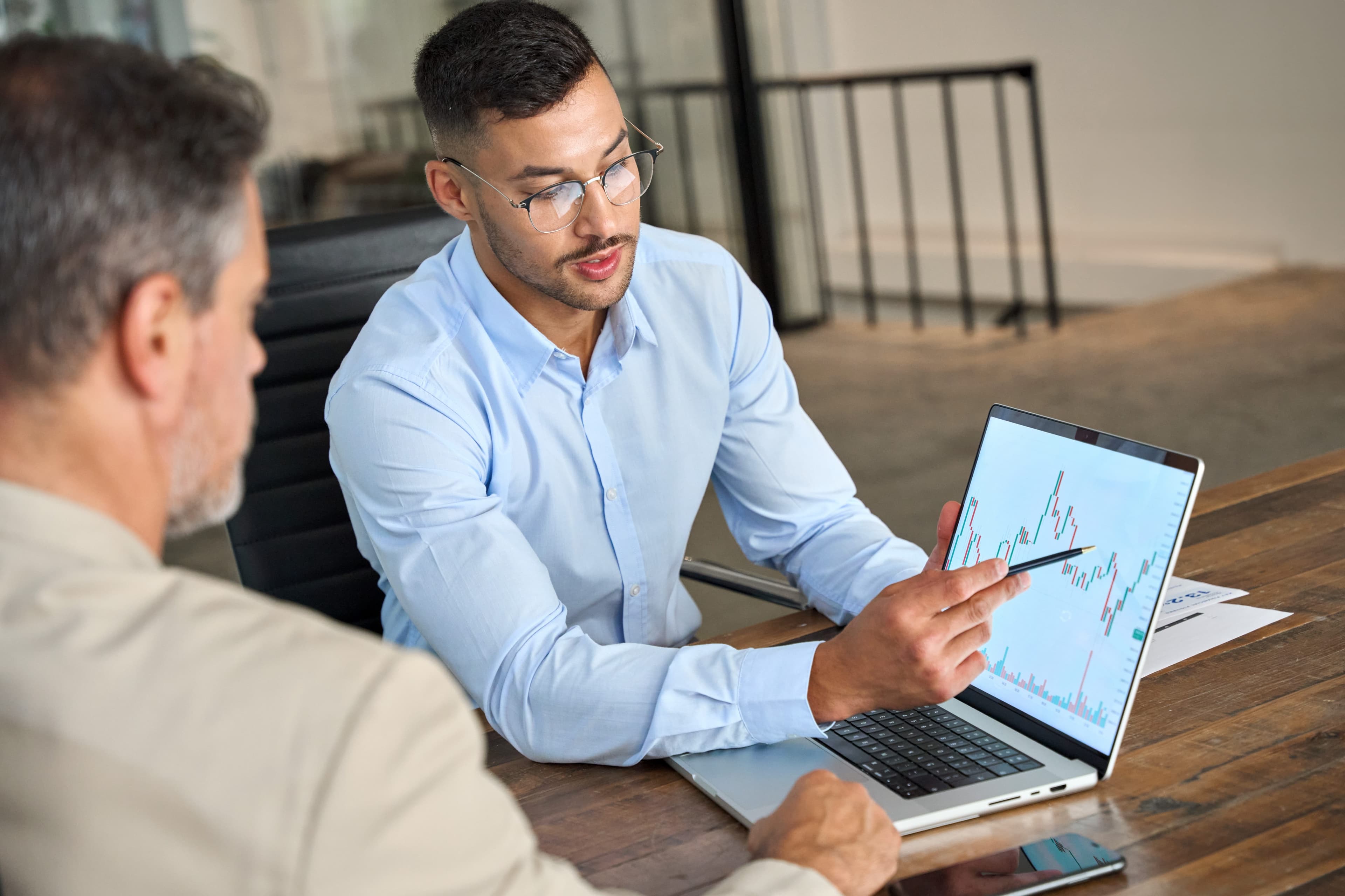 Account manager pointing to a performance chart on a laptop while meeting with a client