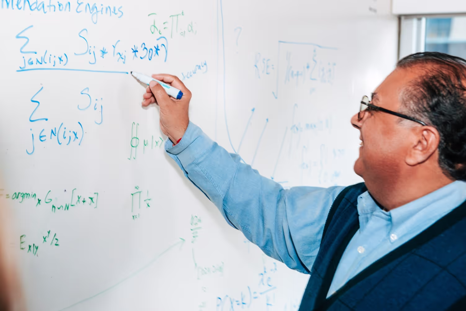 A smiling man writes arithmetic formulas on a whiteboard